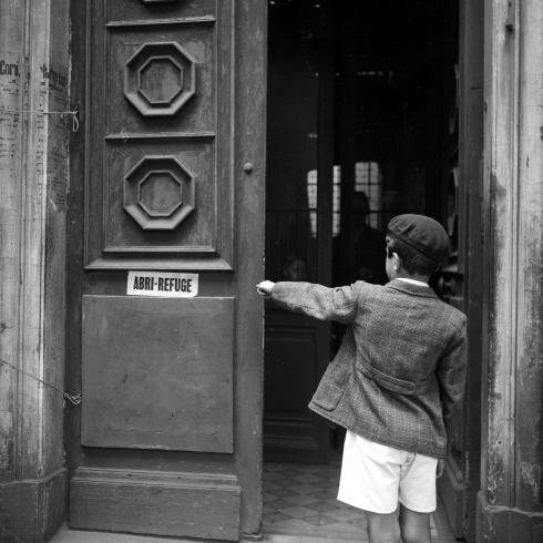 Émile Rougé, un enfant montre du doigt l'inscription "Abri-Refuge" sur la devanture d'une porte